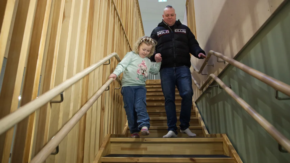 Moa tar sig försiktigt nedför trappan på Råssnäs förskola, pappa Viktor Borger håller i hand och säkrar färden ned mot markplan.