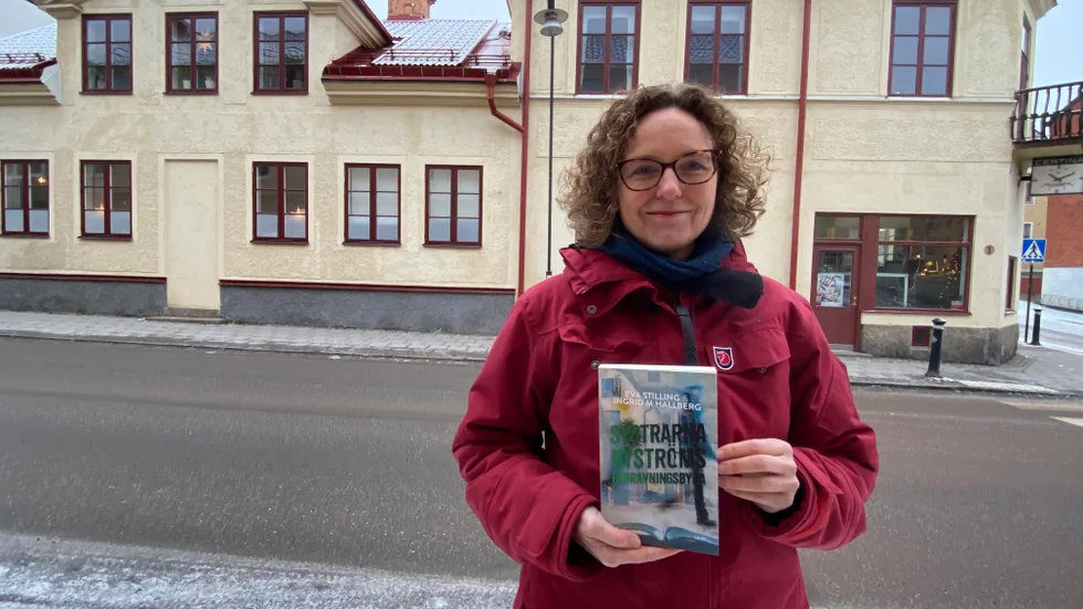 Författaren Eva Stilling från Mariefred på Storgatan i Strängnäs. I det gula huset på andra sidan gatan har hon och medförfattaren Ingrid M Hallberg placerat sin påhittade begravningsbyrå. "Här har vi stått många gånger och funderat och tagit in detaljer", säger Eva Stilling. 