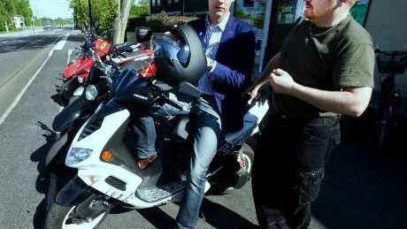 Christofer Fjellner provsitter en EU-moped medan Fredrik Landers förklarar vad han tycker om EU-körkortets prishöjning.            Foto: Titti Olovsson