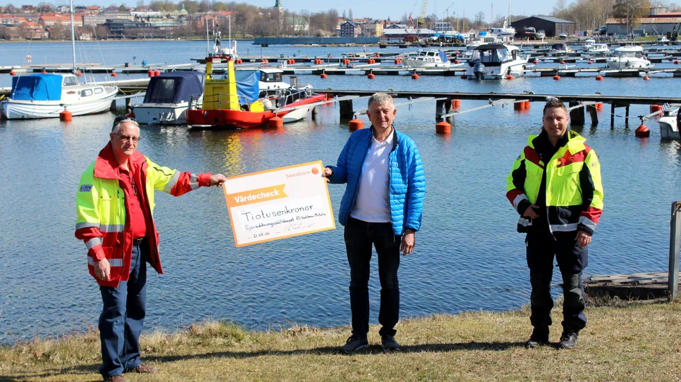 Ola Forslund från Motala Vätternfiskeklubb lämnar över en check till Håkan Andersson och Johan Weber, Sjöräddningssällskapet RS Vadstena-Motala.