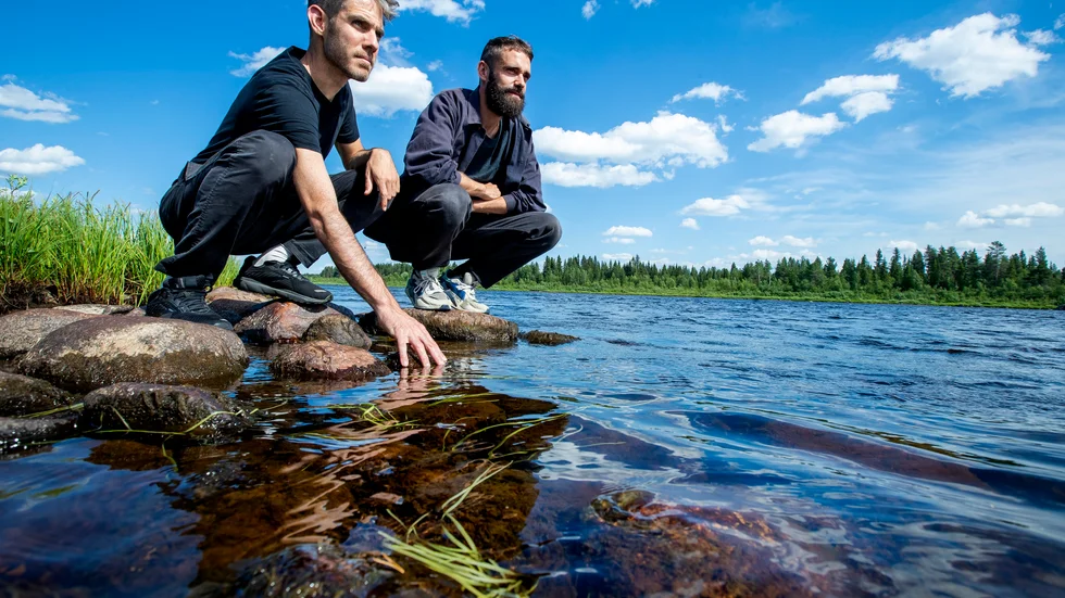 Alon Schwabe och Daniel Fernandez Pasqual känner på vattnet i Lainioälven i Kangos. I två veckor åker de runt för att hämta in material till en utställning hösten 2022. 