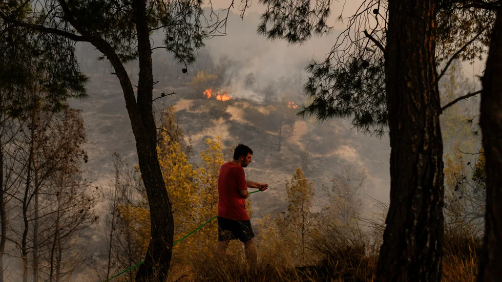 En man försöker släcka en brand väster om Greklands huvudstad Aten.