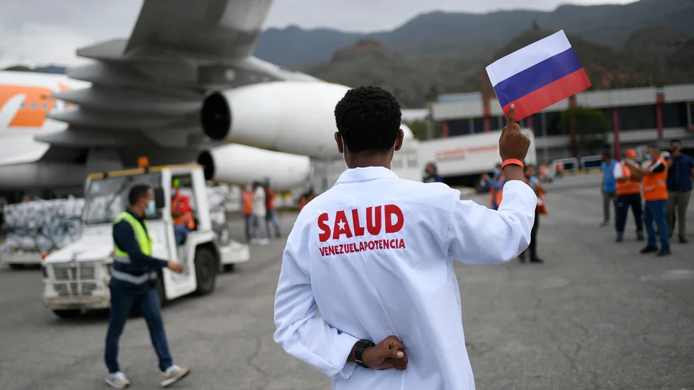 En vårdarbetare håller upp den ryska flaggan medan Sputnik V lastas av ett flygplan i Venezuela – som är ett av de länder som tar emot Rysslands vaccin. Arkivbild.