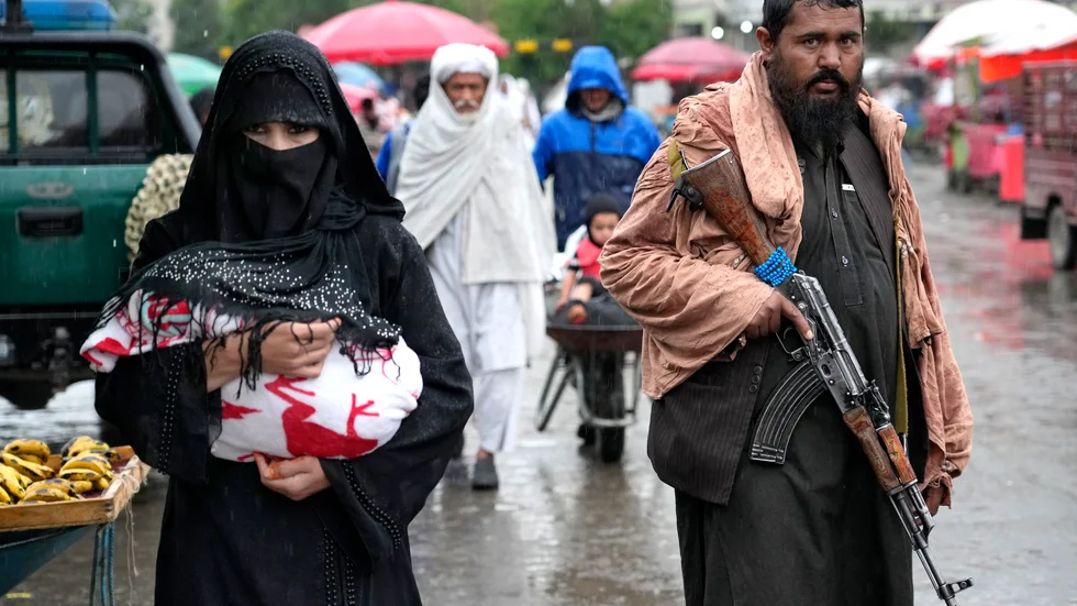 En afghansk kvinna går genom en marknad i Afghanistans huvudstad Kabul och en talibankrigare håller vakt. Arkivbild.