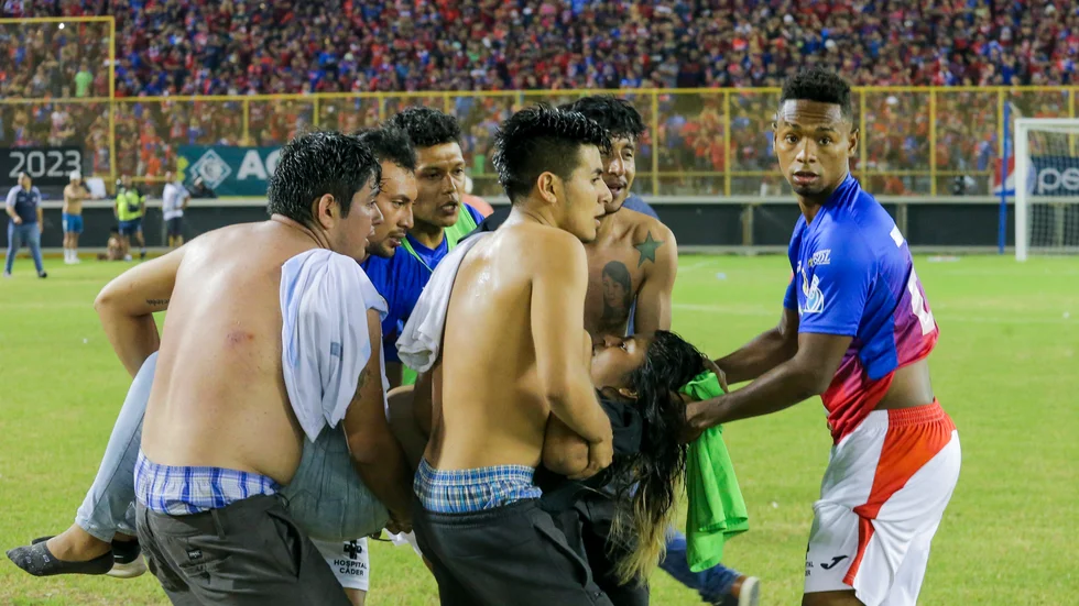 En skadad besökare bärs bort av fotbollssupportrar i Monumental stadium i Cuscatlan.