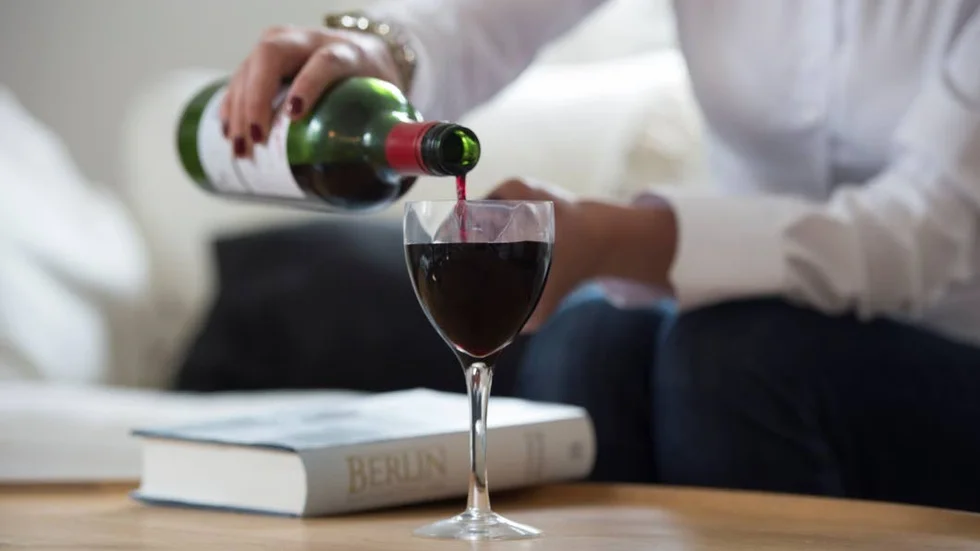 En kvinna kopplar av med ett glas vin och en bok (Arkivbild).