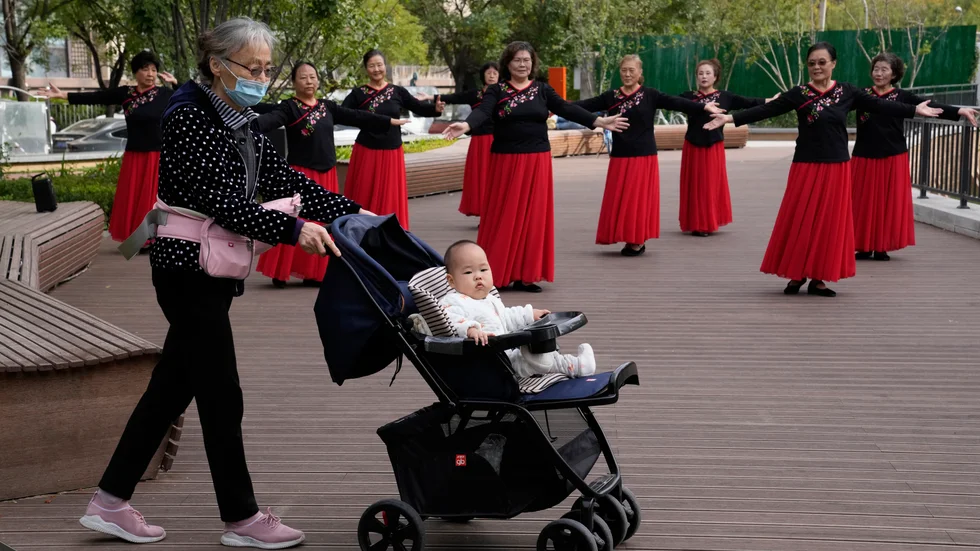 En äldre kvinna kör ett barn i vagn i en park i Peking. Arkivbild.