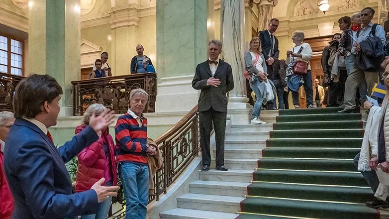 Den nuvarande talmannen Andreas Norlén möter här i det gamla riksdagshusets trappa en skådespelare som föreställer greve Hamilton; talman i första kammaren då Kerstin Hesselgren debuterade i kammaren 1922 efter att ha blivit invald i valet 1921. 