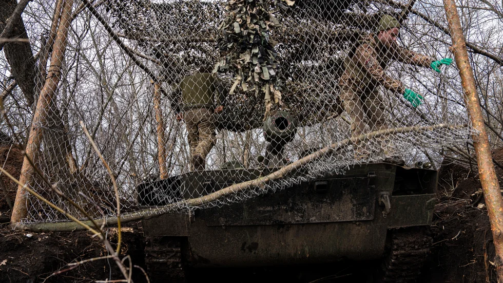 Ukrainska soldater täcker en artilleripjäs för att den ska bli svårare att upptäcka för Rysslands så kallade kamikazedrönare. Bilden togs vid fronten i Bachmut i fredags.