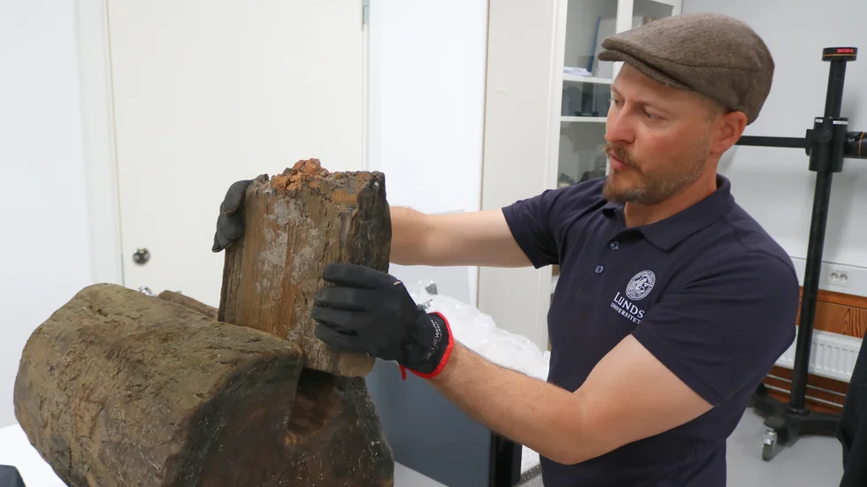 Peter D'Agnan visar hur en plankbit passar in i stocken. Delarna har han tillfälligt tagit upp ur träsket, de ska sedan läggas tillbaka där de togs.