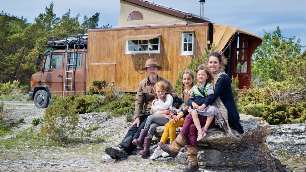 Daan Zuijderwijk och Maaike Vergouwe med döttrarna Alba 6 år, Isolde 4 år, Fenna 8 år och hunden Nan utanför sitt tiny house på hjul, med utfällbar markis vid flaket, sovalkov på taket och fönsterluckor som ger skugga.
