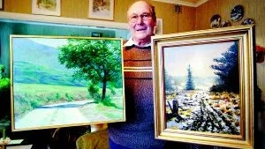 Foto:  ANDERS STEINER Stig Hansson med två av målningarna som lottas ut i det årliga konstlotteriet. Han kommer som vanligt stå och sälja lotter under julmarknaden i Ankarsrum.