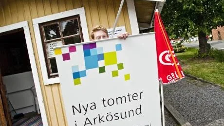 Marcus Söderström rullar upp affischen som ska locka förbipasserande i Arkösund att komma och prata tomtköp.