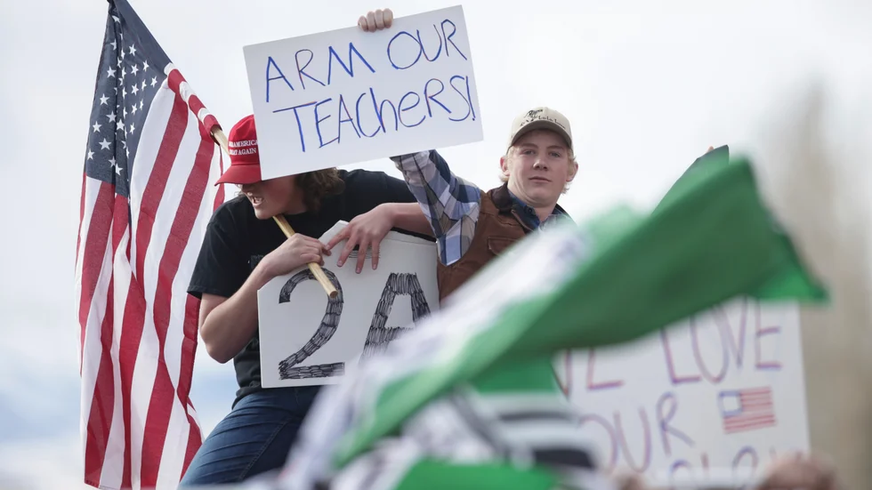 När halva klassen demonstrerar mot vapen väljer den andra halvan att propagera för att även lärarna ska bära vapen - bakom en flagga som associeras med alt-rigt-rörelsen. (John Roark/The Idaho Post-Register via AP)  