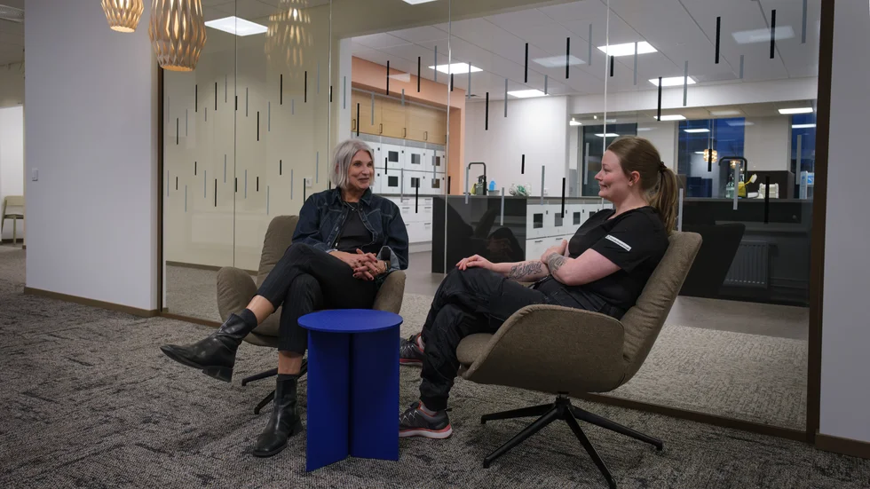 Susanna Henriksson och Michaela Kemppainen tar en paus i en av sittgrupperna som finns på flera ställen i huset. Bakom glasväggen ser man en del av lunchrummet.