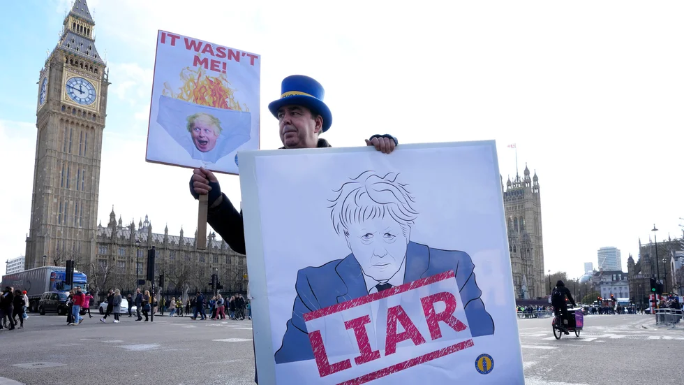En demonstrant håller upp ett plakat utanför parlamentet i London, där tidigare premiärministern Boris Johnson fick svara på anklagelser om att han vilselett parlamentet angående sin kännedom om brott mot pandemilagarna. Arkivbild.