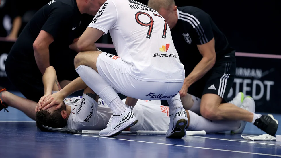 Albin Sjögren håller sig för ansiktet efter att ha skadat knäet. Lagkamraten Robin Nilsberth kollar läget med Sjögren får behandling.