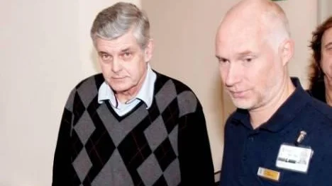Förre polischefen Göran Lindberg leds in i rättssalen av en vakt.