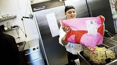 Patrik Söderman, chefskock på Uplands, häller pommes i fritösen. Till vänster i bilden skymtar Imran Iqbal förbi.