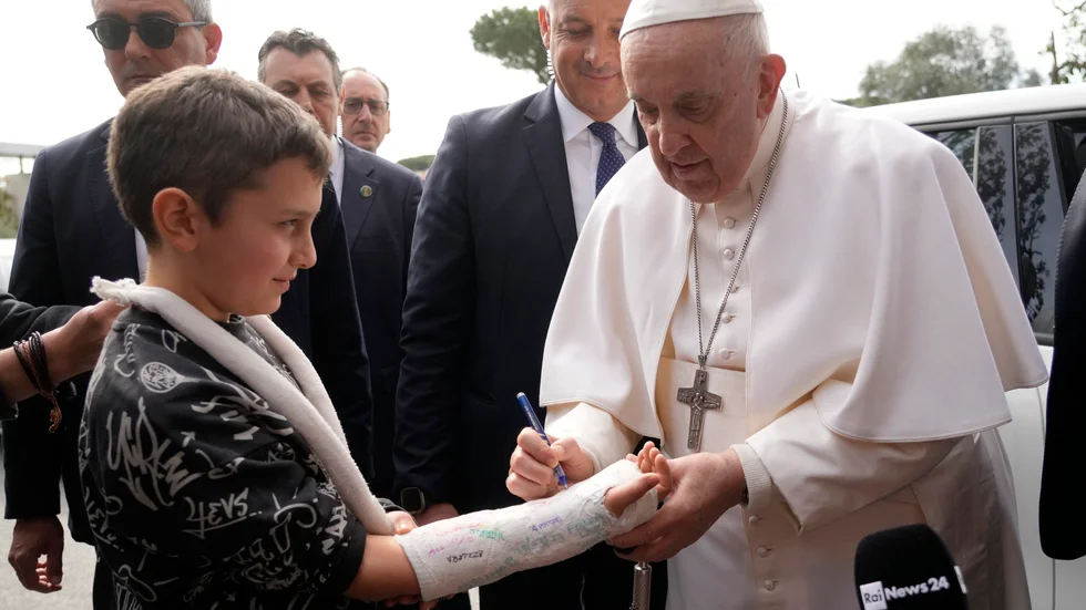 Påve Franciskus signerar en pojkes gips i samband med att han lämnar sjukhuset på lördagsförmiddagen.