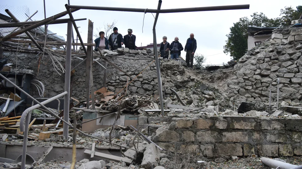 En grupp män granskar rasmassorna som återstår av ett bostadshus i Stepanakert på söndagen.