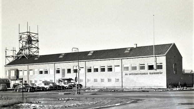 Taknocken på ICA:s 1956 invigda lagerbyggnad på Industrigatan 15 pryddes med ett snurrande ur. Mitt i uret fanns lagrets emblem, SV, som stod för Speceristernas Varulager.