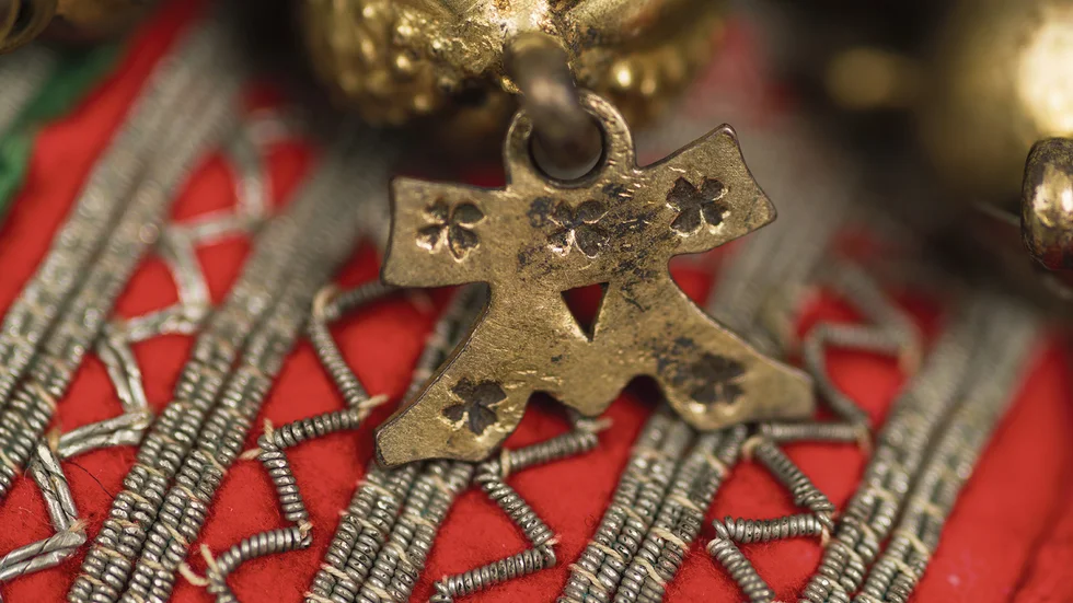 Ett Ave Maria-hänge från en samisk silverkrage. Ave Maria-hängen och monogram av silver har katolsk bakgrund och symboliserade under medeltiden jungfru Maria. De förekommer rikligt inom den samiska formvärldeb och återfinns som dekoration på silverföremål som bägare, skedar och silverkragar. Detta fynd kommer från Lule eller Pite lappmark.