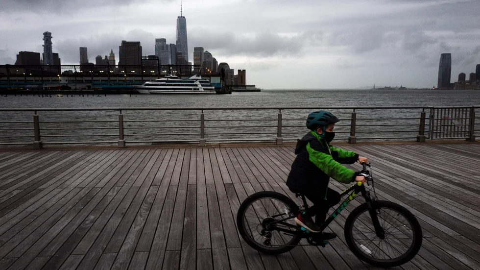 En pojke med ansiktsmask är ute och cyklar i Hudson River Park, New York. Pojken har inget med texten att göra.
