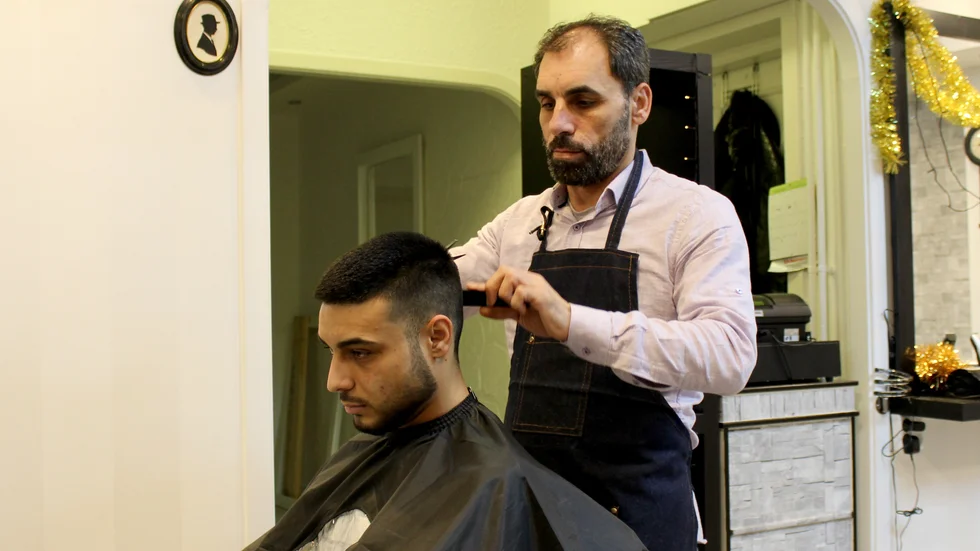 Bassam Al-Deek lär upp sin son Mohammed-Baraa Al-Deek, som här sitter i stolen, inom frisöryrket. 